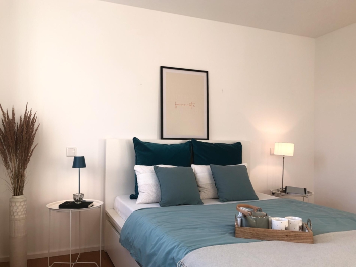 modernes Schlafzimmer mit weißem Bett und Kissen und Details in Petrol und Aqua