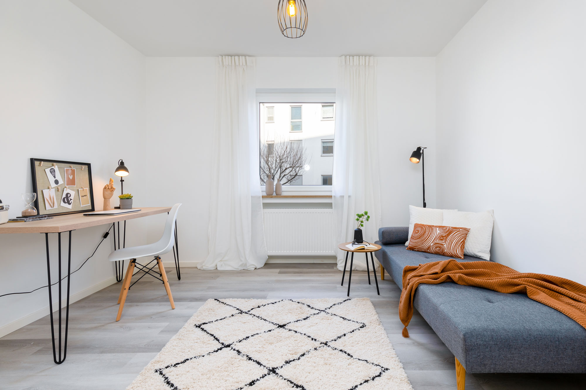 Ein von elements Home Staging für den Immobilienverkauf vorbereitetes Arbeitszimmer mit grauer Couch und Arbeitstisch.